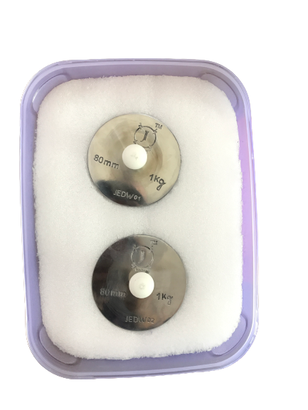 person writing in a notebook beside by an iPad, laptop, printed photos, spectacles, and a cup of coffee on a saucer